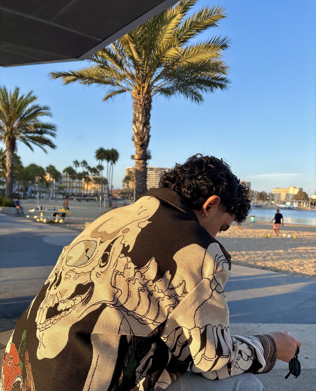 Daniel seated at the waterfront in a skeleton-print jacket, head lowered