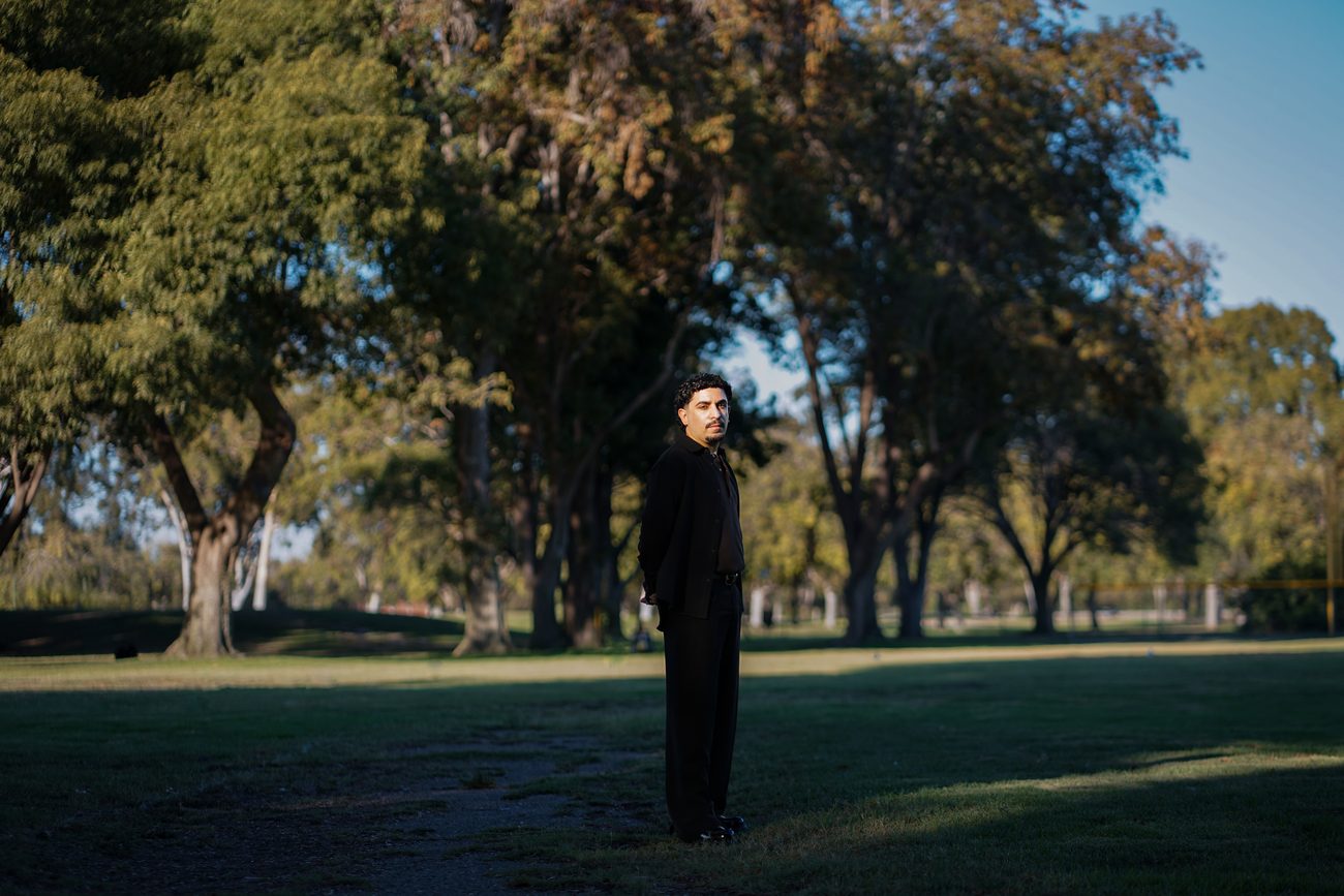 Daniel standing among tall trees in a park at golden hour