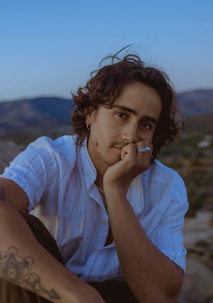 Sagrados mood image — young man resting his chin on his hand, hills behind him at dusk